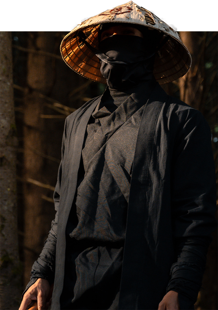 Person wearing a dark coat and straw hat in a forest setting